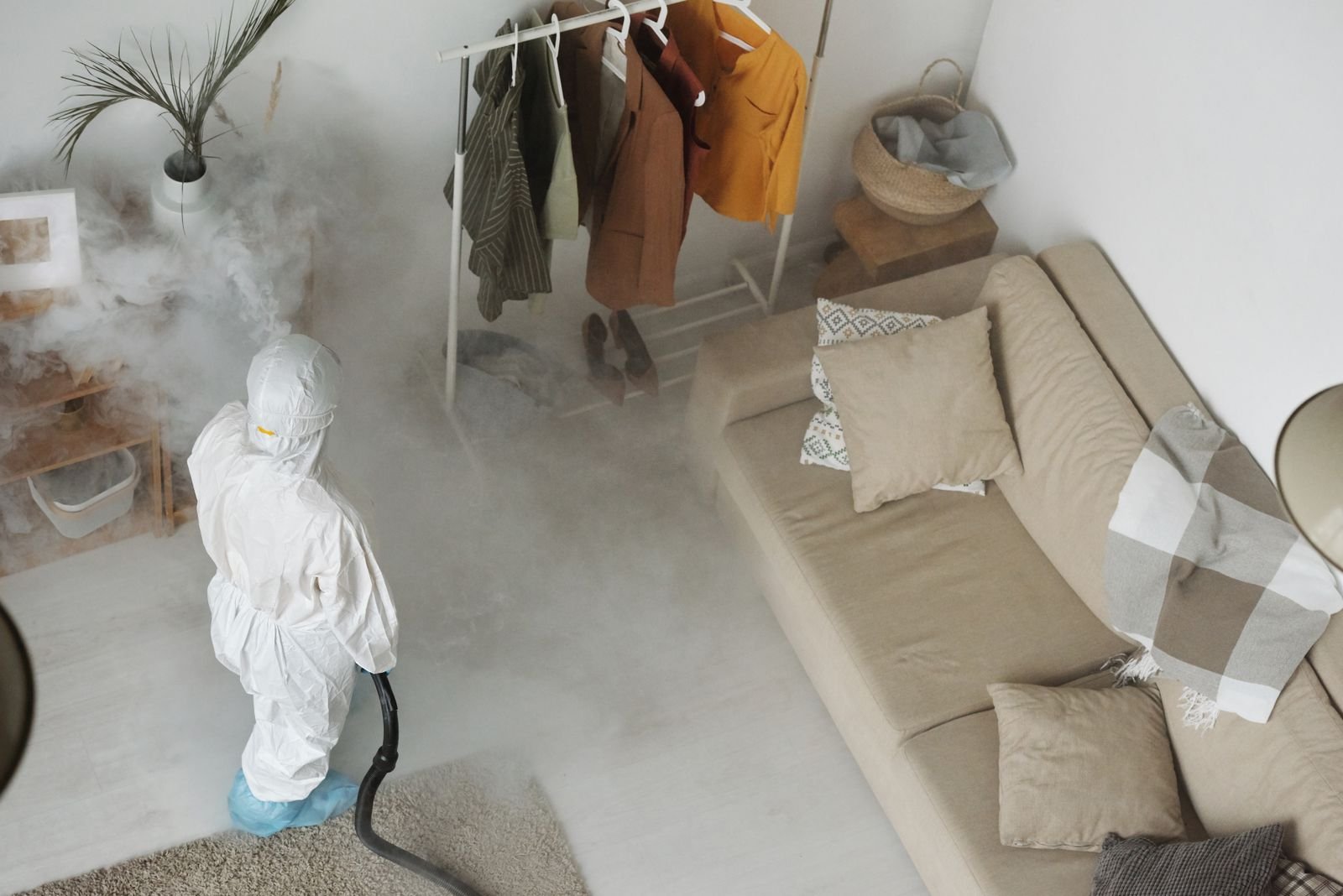 Désinfection par nébulisation Intervenant en tenue de protection traitant l'air d'une pièce avec un appareil de nébulisation.
