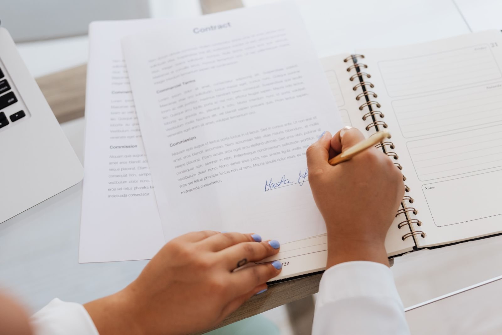 Devis écrit et pièces du dossier Mains signant un document sur un bureau, stylo et fournitures posés à côté.
